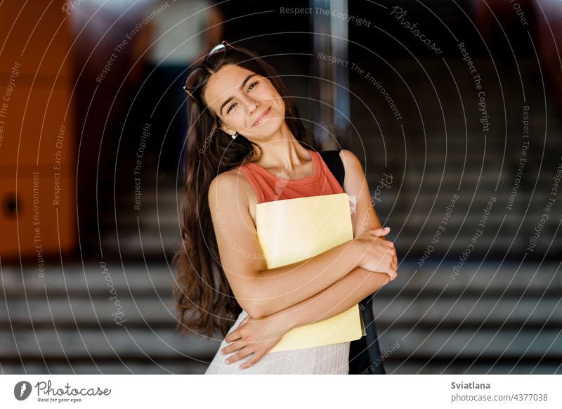 Portrait of a smiling girl with a folder in her hands student steps holding bag young university stairs glasses outdoor college woman teenager female studying