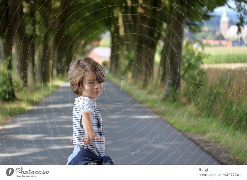 Boy stands on an avenue, looks and points to the photographer Human being Child Boy (child) Infancy Street Avenue Tree To go for a walk out In transit