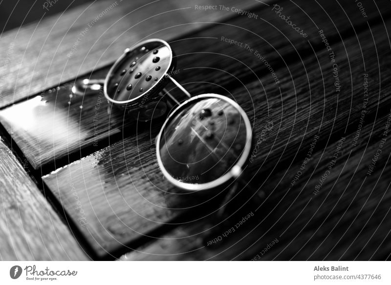 Black and white shot of a pair of sunglasses on a rain-soaked table with raindrops on the lenses. Sunglasses Eyeglasses Summer Rain Wet Drops of water Detail