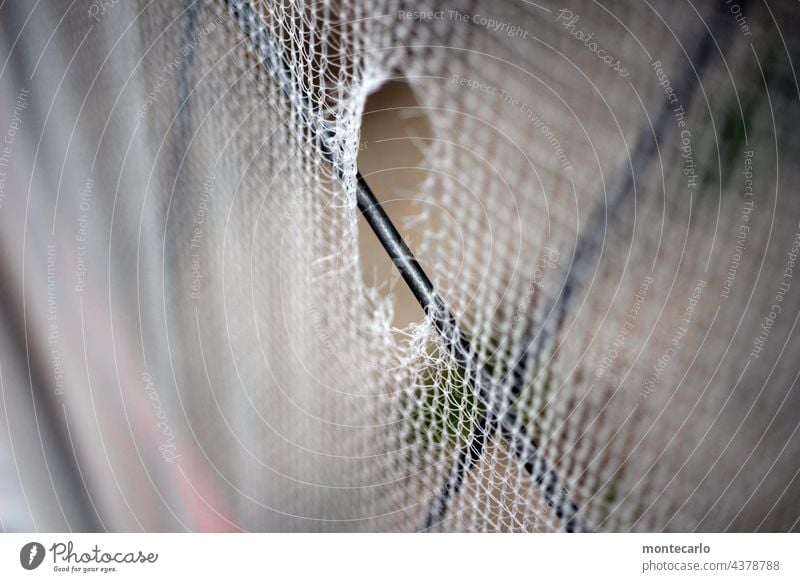 A peephole in the construction fence cover Peephole damage Construction fence cover weave Broken Hoarding Iron Abstract Gray Plastic Close-up Protection Safety