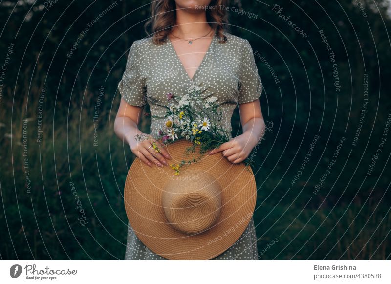 A young girl holds a hat and a bouquet of wildflowers in her hands. dress summer summer evening sun daisies field romance femininity tenderness