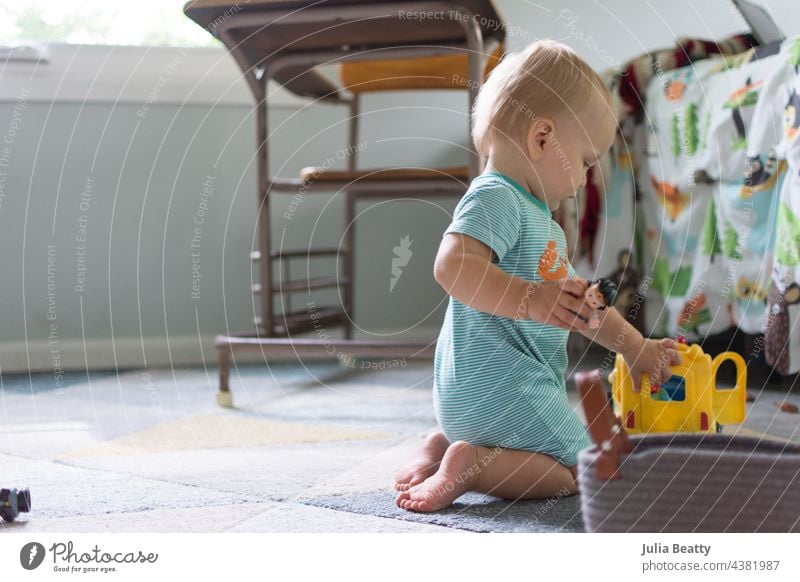 14 month old baby plays with a school bus toy and figurines; child's bedroom and vintage desk in background independent play put in take out childhood