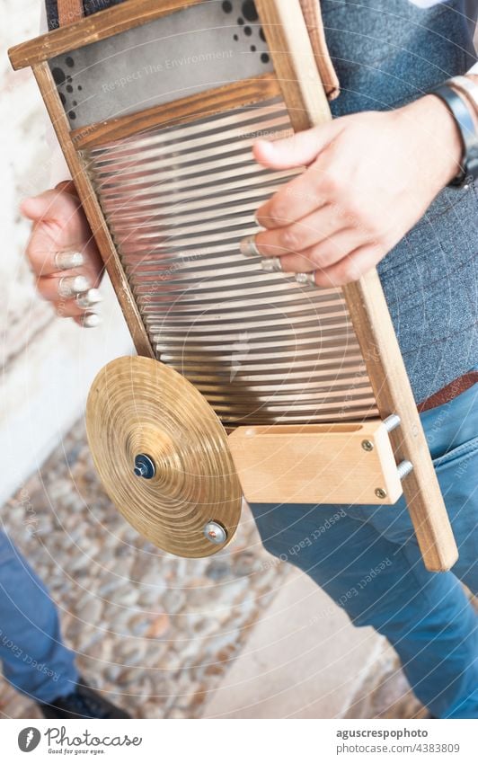 Close-up of a man playing a jazz instrument on a washboard in the street. The instrument is seen, along with the cymbal, the wood and the thimbles with which it is played.