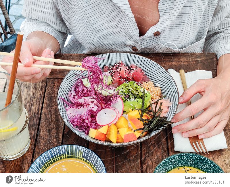 Woman eating tasty colorful healthy natural organic vegetarian Hawaiian poke bowl using asian chopsticks on rustic wooden table. Healthy natural organic eating concept