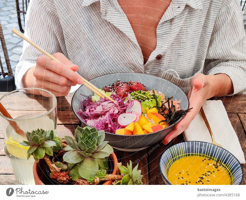 Woman eating tasty colorful healthy natural organic vegetarian Hawaiian poke bowl using asian chopsticks on rustic wooden table. Healthy natural organic eating concept