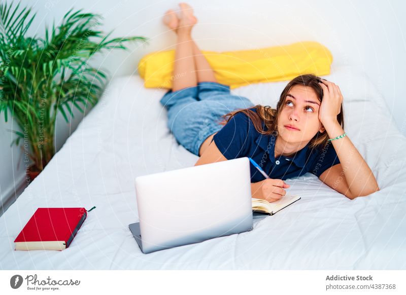 Young woman studying online in bedroom student write laptop at home remote education gadget female young teen teenage take note internet device smart assignment