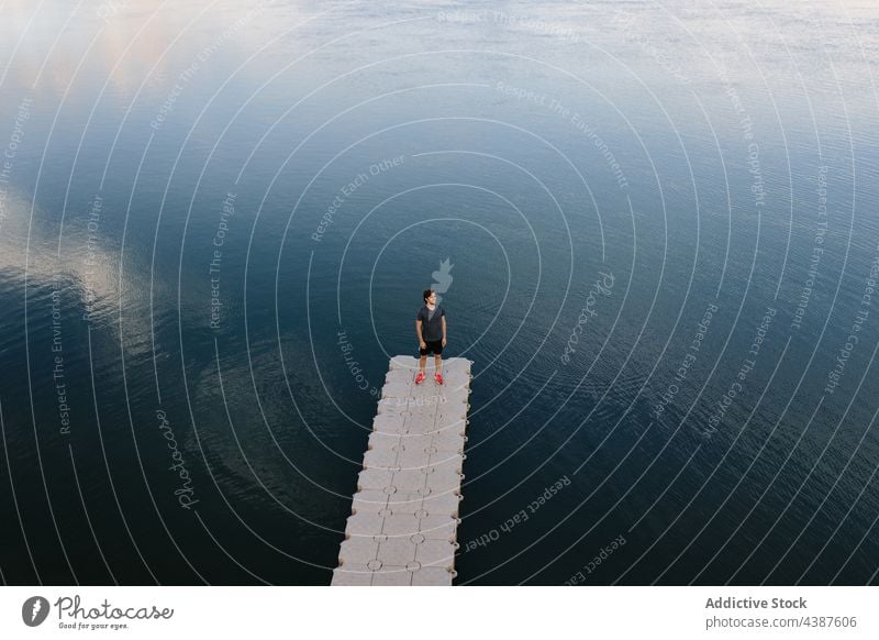 Man standing in pier near lake man calm pond quay shore serene peaceful tranquil male nature water coast edge scenic reflection mirror surface aqua idyllic