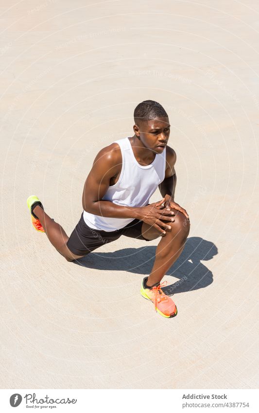 Black sportsman stretching legs during workout in summer black warm up training lunge exercise athlete flexible male african american ethnic wellness sportswear