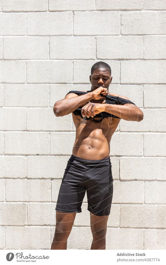 Muscular black sportsman putting on tank top in street put on fit torso strong muscular athlete sportswear city male ethnic african american wellness confident