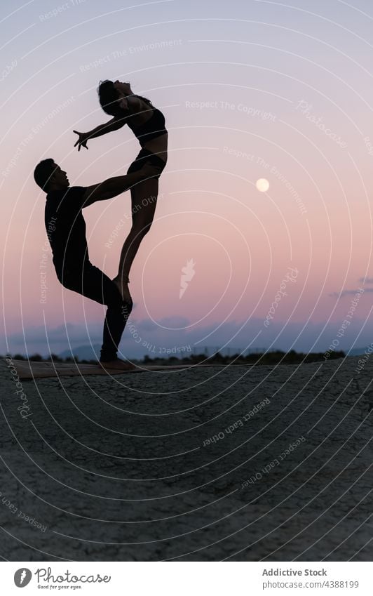 Silhouette of couple doing acroyoga against sunset sky acro yoga balance partner silhouette together practice acrobatic holding hands pose support sundown