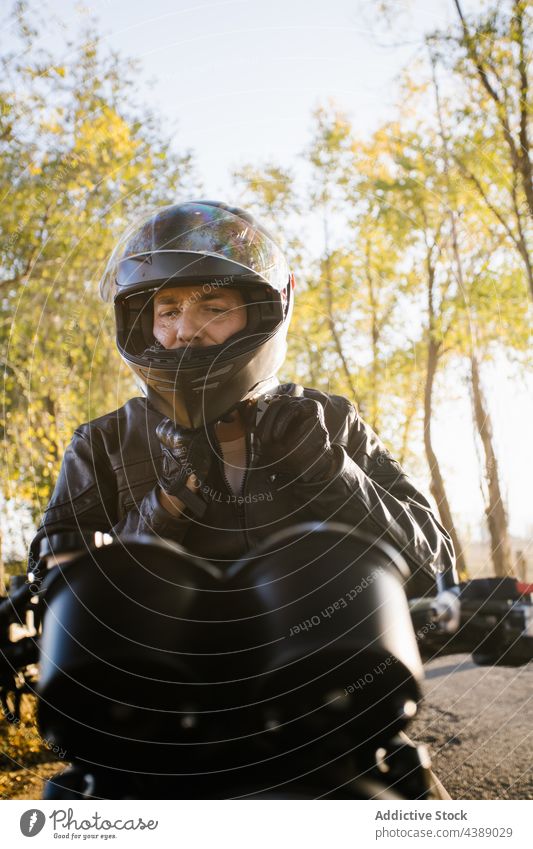 Focused Mature Male Biker Preparing For Riding In Sunny Day helmet motorbike biker man rider action active adventure autumn blur brutal countryside danger drive