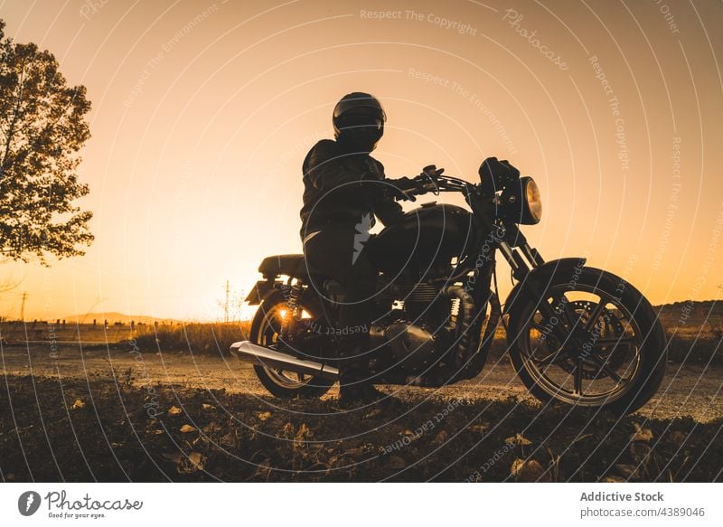 Unrecognizable Racer Driving Motorbike In Sunset In Rural Location biker sunset motorbike shadow helmet road travel active adrenaline adventure anonymous