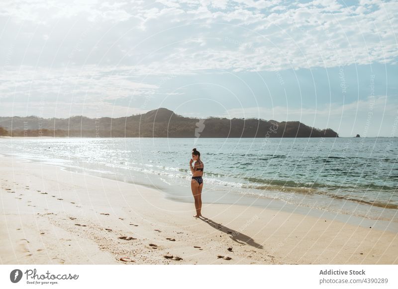 Young woman standing on sandy beach ocean alone summer sunlight nature travel sea female vacation coast young seashore holiday wave bikini seaside traveler