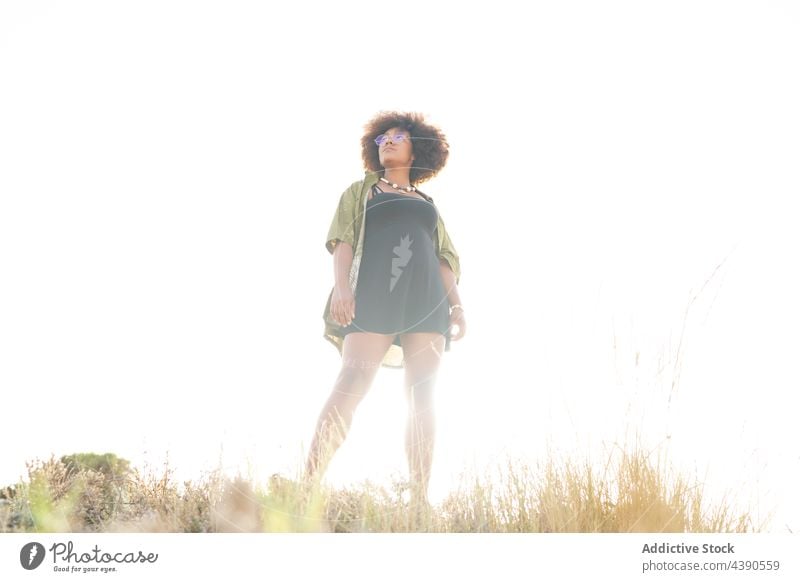 Stylish black woman on sandy beach summer style eyeglasses curly hair dreamy sunlight nature trendy eyewear necklace bijouterie spectacle afro african american