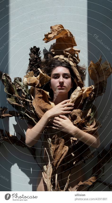 Portrait of a young sexy woman with brown hair artfully decorated covered by leaves of dry, withered banana tree, looking like an art nouveau girl, foliage