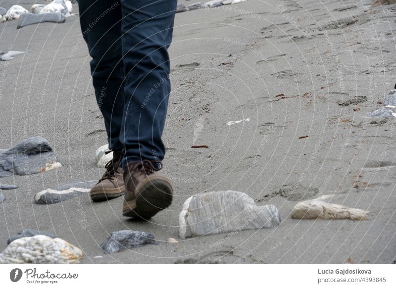 Man walking on sandy beach. He is wearing boots. Only his legs are visible. He is approaching to the camera. There is a lot of copy space. active adult alone