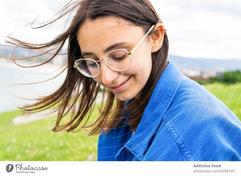 Content woman sitting on hill against sea enjoy seaside cloudy admire smile seafront harmony female nature sky green ocean cheerful happy coast shore freedom