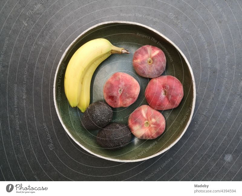 Round fruit bowl with banana, peach and avocado on grey concrete floor in a designer apartment in Rudersau near Rottenbuch in the district of Weilheim-Schongau in Upper Bavaria