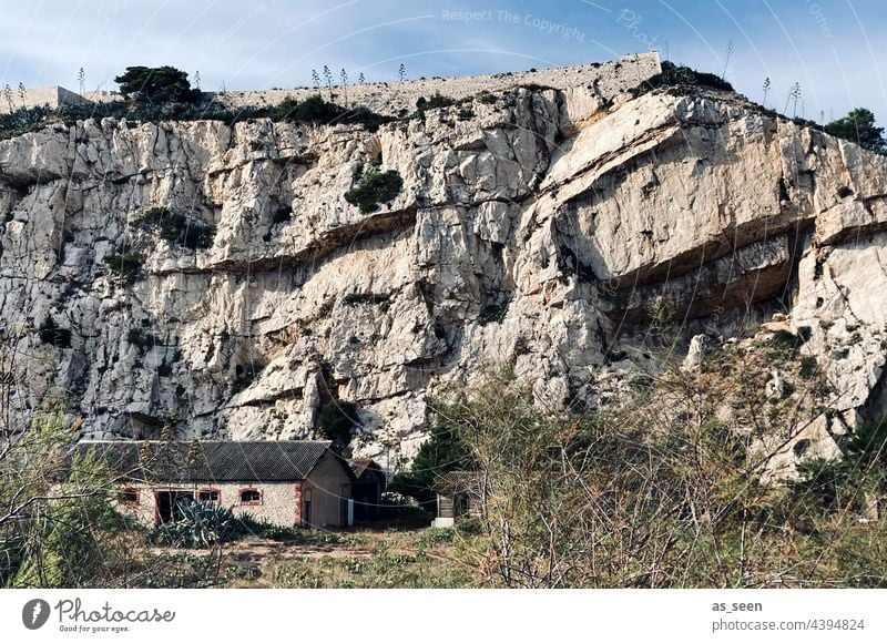 Rock face with house rock stone House (Residential Structure) Small Sky Light Dry undergrowth Massive antagonistic Gray rock strata Exterior shot Colour photo