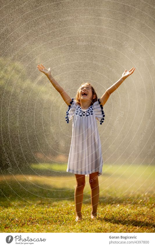 Cute little girl having fun under irrigation sprinkler happy kid summer happiness joy spray wet active water outdoor splash child activity young freedom leisure