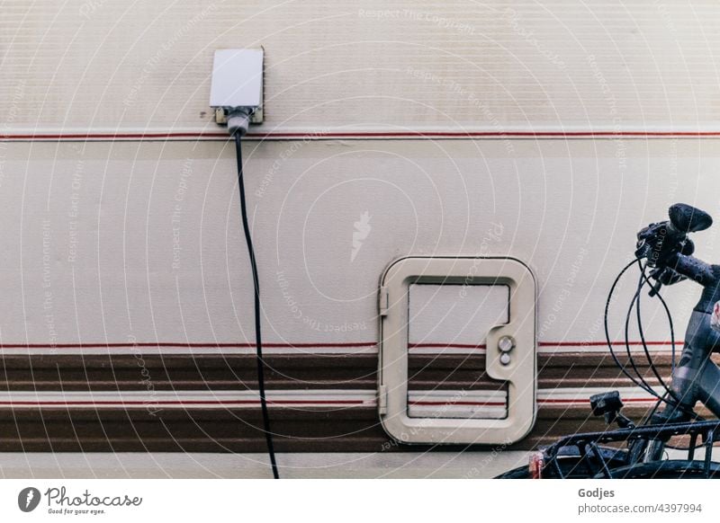 Side view of a caravan with power connection and service flap, bicycle in front of it Caravan Camping site Vacation & Travel Mobile home Tourism Colour photo