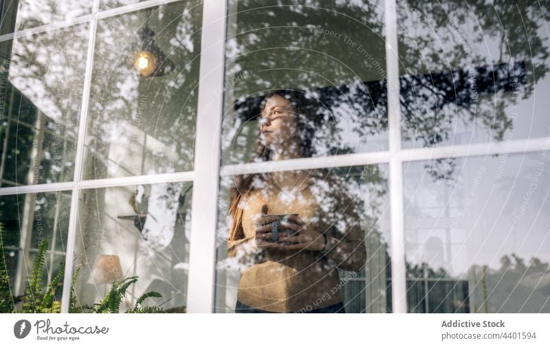 Reflective woman with hot drink looking out window at home look out wistful reflective dreamy alone reflection beverage cup solitude pensive contemplate