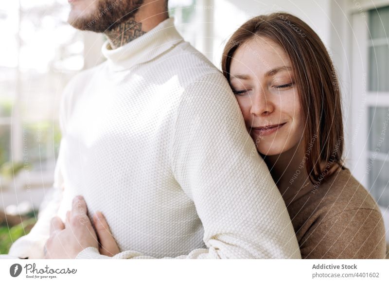 Smiling woman embracing tattooed boyfriend at home couple embrace love relationship romantic contemplate window house cheerful interact mug hot drink beverage