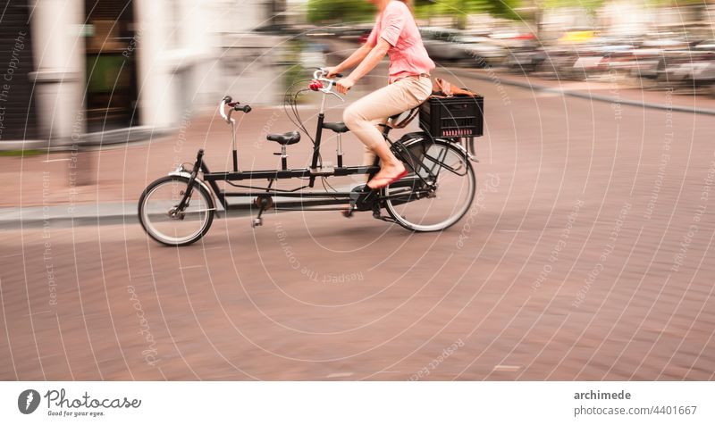 Woman riding a double passenger bicycle in Amsterdam amsterdam bike cargo carry city commuter commuting cycling cyclist day dutch lifestyle motion park people