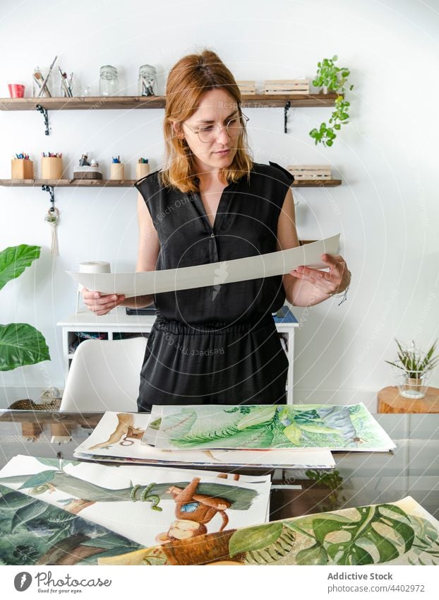 Female designer looking at paintings at table in workspace woman artist project assorted various creative female professional workplace occupation job skill