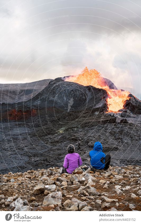 Faceless tourists contemplating active volcano from mountain under cloudy sky admire erupt burn fire nature energy highland fagradalsfjall iceland travel