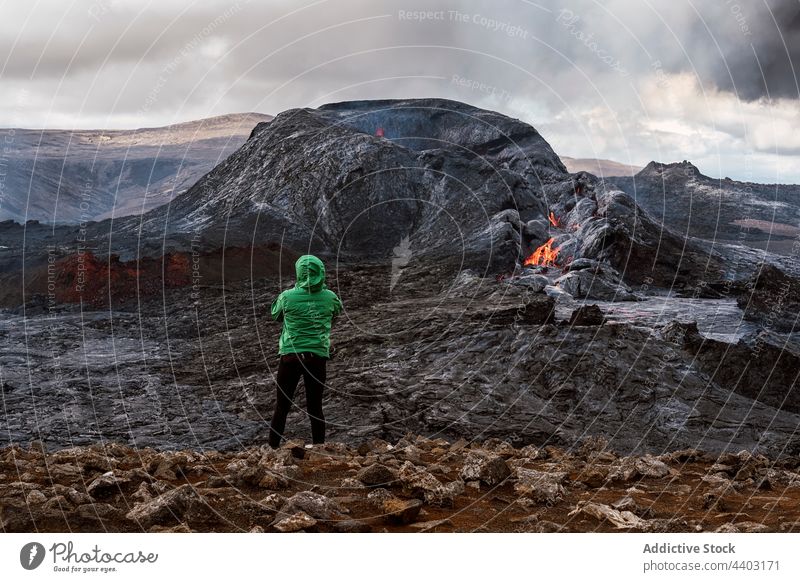 Anonymous tourist admiring erupting volcano under cloudy sky traveler admire burn mount nature highland fagradalsfjall active iceland landscape tourism scenic