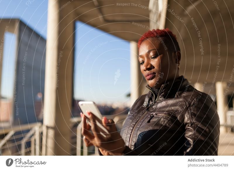 Afro woman browsing by her smartphone black afro ethnic app typing girl trendy looking lifestyle adult candid background using urban cell portrait holding