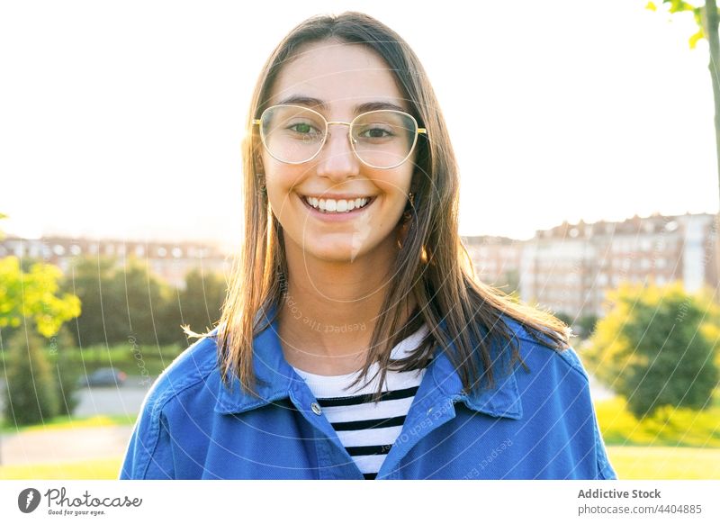 Content woman in stylish outfit on hill in city trendy style sunny urban young smile female content positive happy green meadow lawn sunlight sunshine carefree