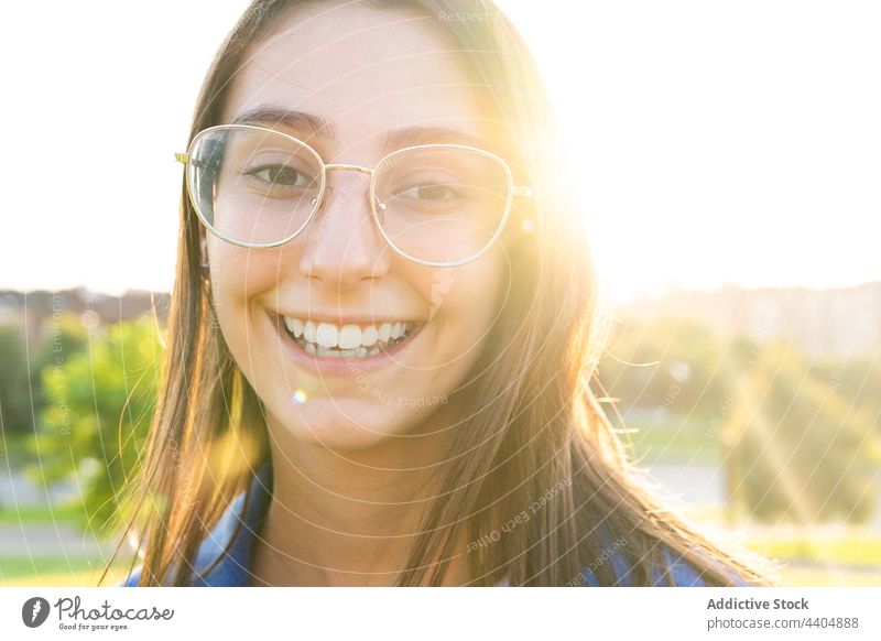 Content woman in stylish outfit on hill in city trendy style sunny urban young smile female content positive happy green meadow lawn sunlight sunshine carefree