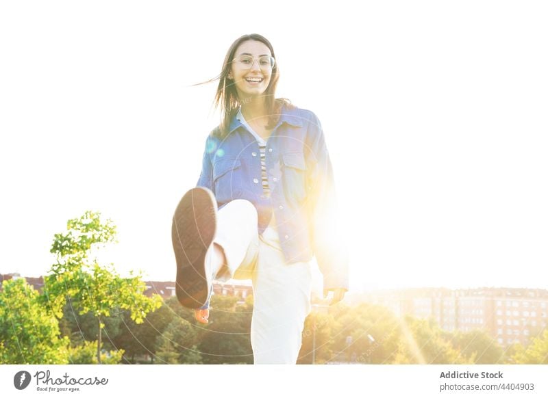 Delighted woman outstretching leg at camera kick cheerful city having fun smile urban sunny female style trendy outfit positive joy charming cool happy glad