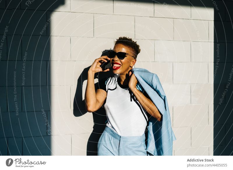 Trendy ethnic woman in sunglasses talking on smartphone on street fashion style sticking out tongue individuality cool haircut using gadget device speak stylish