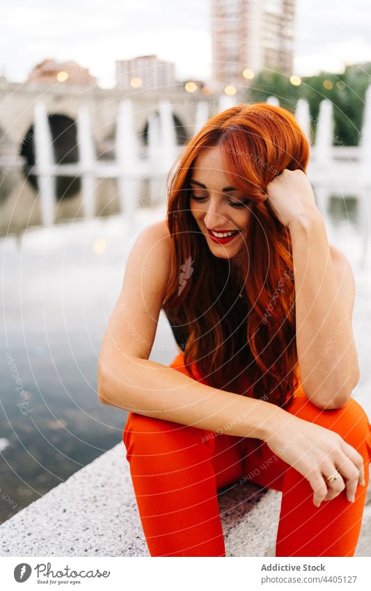 Trendy redhead woman on embankment in city style trendy pants orange bright color female lean on hand vivid vibrant positive happy smile cheerful urban enjoy