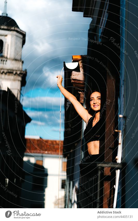 Cheerful woman enjoying sunset on balcony of building sunlight stretch serene carefree sundown stick out female smile city cheerful eyes closed arms raised