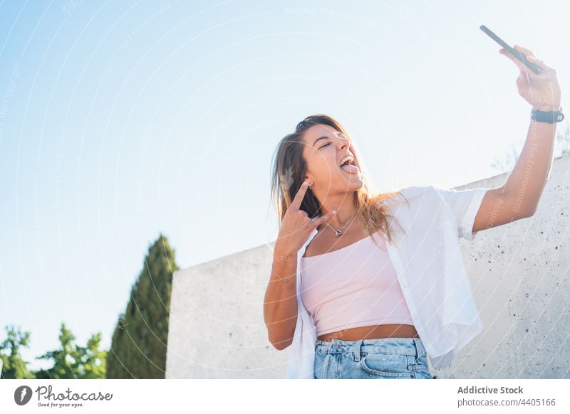 Smiling woman taking selfie in street smartphone city summer self portrait moment female happy cheerful memory mobile device tongue out smile sticking