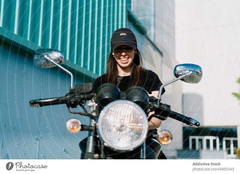 Cheerful woman sitting on motorbike and looking at camera motorcycle biker motorcyclist cheerful parked city smile rider female transport vehicle urban street