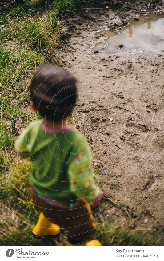 boy wearing rubber boots stands in front of puddle of mud boys carefree caucasian ethnicity child childhood cute day enjoyment fun happiness horizontal