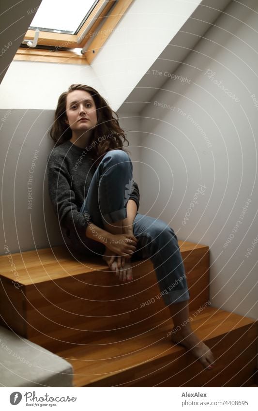 Portrait of a young woman sitting barefoot in jeans and sweater and a skylight looking into the camera Woman Young woman Brunette long hairs Long-haired pretty