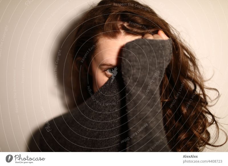 Portrait of a young woman who pulls her grey knitted sweater in front of her face and looks into the camera with only one eye Woman Young woman Brunette