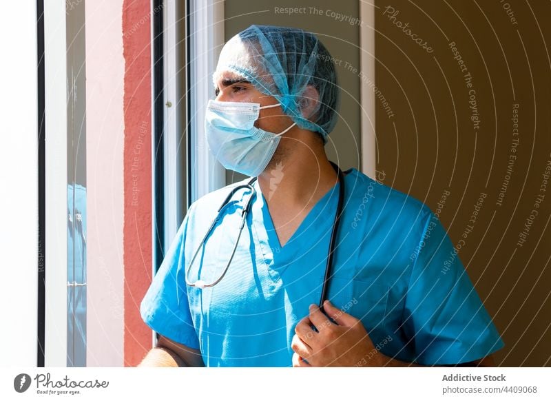 Male doctor standing in hospital with hat and face mask break medic clinic uniform tired health care man workday male job medical pause professional occupation