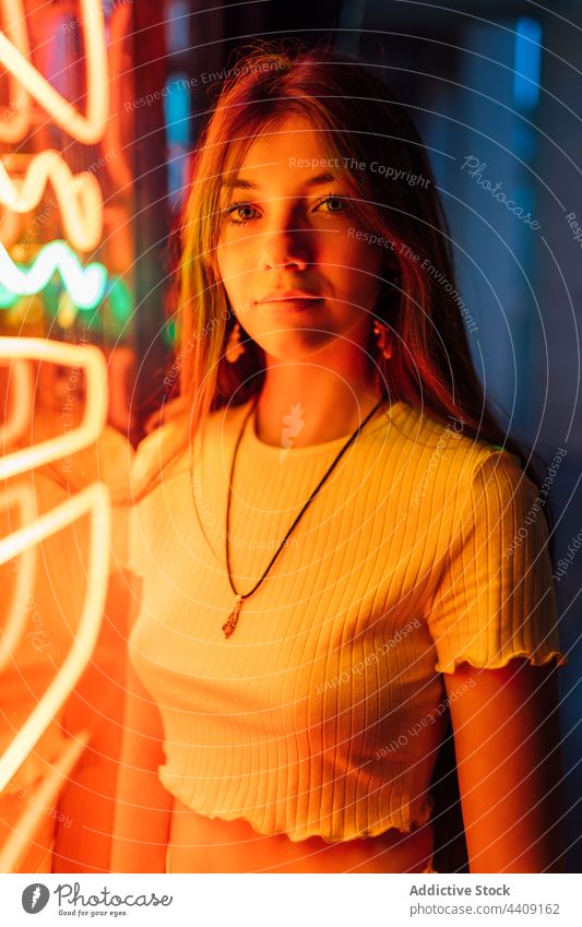 Tender woman illuminated on neon lights wall at night orange glass wall sincere gentle sensitive alone gaze portrait dusk deep tilt reflection pleasant evening