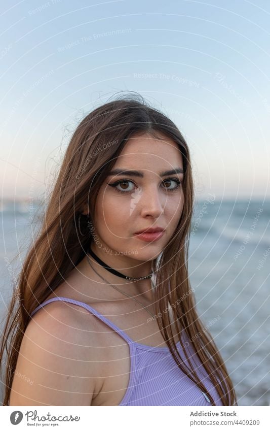 Young woman standing near sea beach wave evening dreamy coast seaside summer weekend female rest young water shore ocean relax long hair wavy hair feminine slim