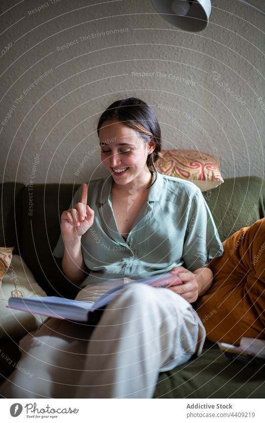 Smiling woman reading a book at home sofa smile female happy cheerful sit weekend enjoy glad living room fondness delight tender content optimist sincere gentle