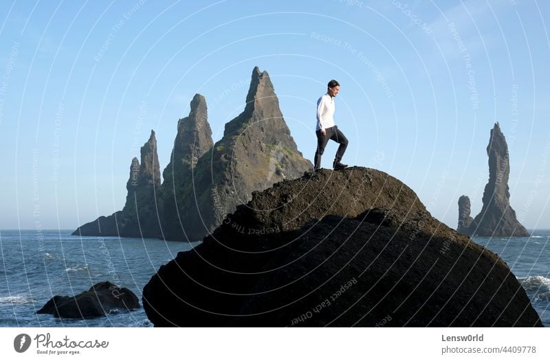 Man standing on a rock at Reynisfjara Black Beach, Iceland, with wind in his hair adventure black beach blue cliff concept freedom handsome hiking hill iceland