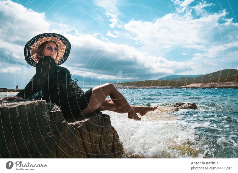 Amazing view of a brunette sitting on a rock near the sea. Amazing summer weather in Croatia , vis island. Sunbathing in the sun with waves hitting the shore