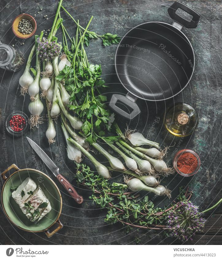 Empty black pan and  variety of fresh herbs for cooking on dark rustic table with knife, cheeses, olive oil and spices. Home kitchen. Top view empty